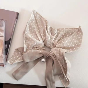 Close-up of beige polka dot bow hair tie with a hanging pearl charm and soft fabric