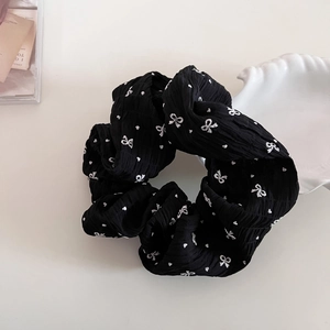 Gros plan d'un chouchou en tissu plissé noir avec broderie de nœuds blancs et de cœurs