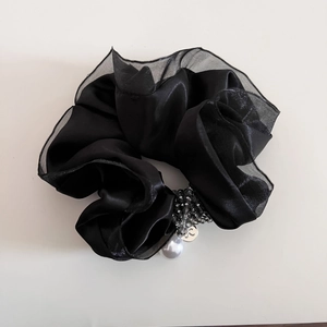 Dettaglio di elastico in raso nero con perline grigie e un ciondolo a perla bianca