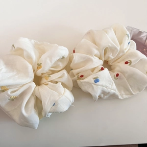 Detailed macro view of two beige scrunchies featuring colorful floral embroidery on fabric