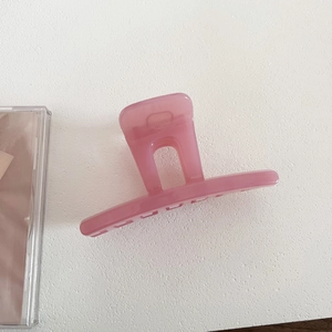 Top-down macro view of a translucent pink resin hair claw clip on white textured surface