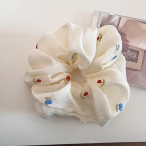 Detail of beige scrunchie with colorful floral embroidery and textured fabric finish