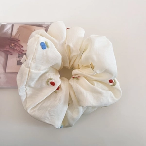 Close-up of beige scrunchie with colorful floral embroidery and textured fabric
