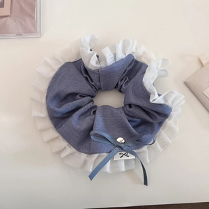 Close-up of blue denim scrunchie with white pleated ruffle edges and handmade charm