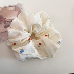 Detailed view of beige scrunchie with red and blue floral embroidery and textile texture