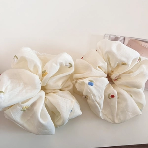 Close-up detail of cream embroidered floral scrunchies with delicate cherry and leaf patterns