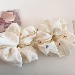 Detail of two beige scrunchies with floral embroidery and soft textured fabric