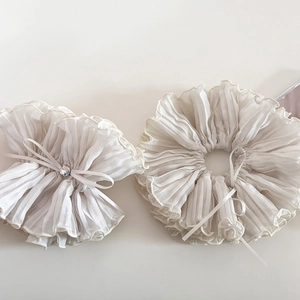 Close-up of pleated cream chiffon scrunchie with delicate rhinestone bow and soft texture