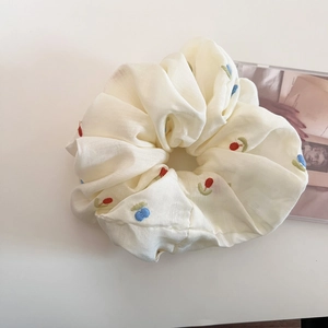 Close-up of beige scrunchie featuring delicate floral embroidery and textured fabric