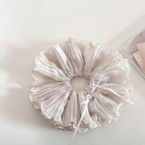 Close-up of pleated cream scrunchie with rhinestone bow detail and elegant wavy edges