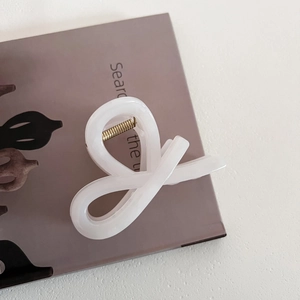 Close-up of minimalist white matte hair claw clip with golden spring on a textured background