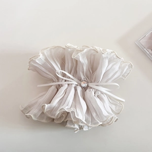Detail of a creamy white organza scrunchie with layered ruffles and crystal bow accent