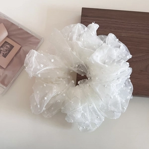 Macro view of white oversized mesh hair scrunchie with textured polka dots on a wood surface