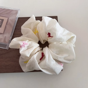Minimalist beige embroidered floral scrunchie hair tie on a rustic wooden board
