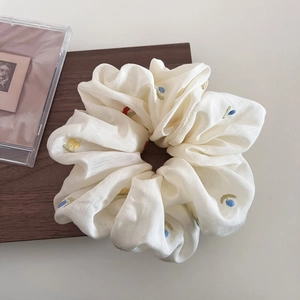 Macro detail of beige scrunchie featuring colorful floral embroidery on cotton fabric
