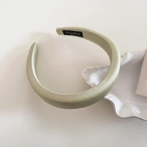 Close-up of sage green satin headband with tiny rhinestones near a white shell dish