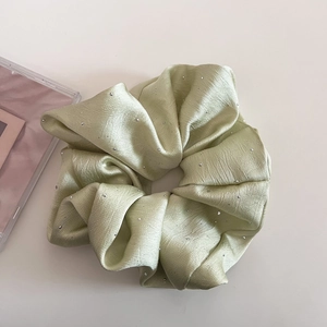 Detail von mintgrünem Satin-Haargummi mit glitzernden Strasssteinen und seidigem Glanz