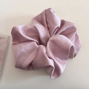 Nahaufnahme von rosa Satin-Haargummi mit glänzenden Strasssteinen und seidiger Textur