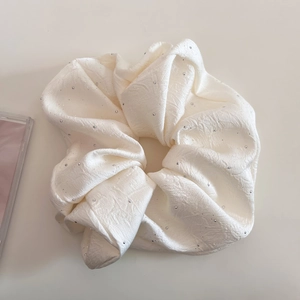 Nahaufnahme von cremefarbenem Satin-Haargummi mit glitzernden Pailletten und Faltenstruktur