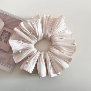 Detail eines eleganten plissierten Satin-Haargummis in Champagner mit weißen Perlen