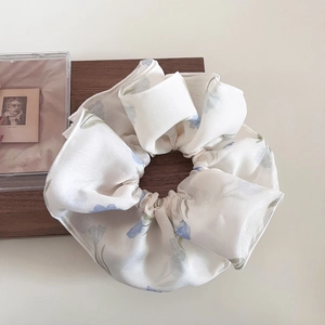 Dettaglio di scrunchie crema con stampa floreale azzurra in tessuto di organza
