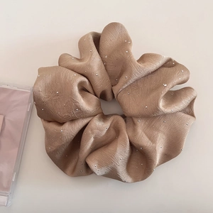 Detail von champagnergoldenem Satin-Haargummi mit glitzernden Strasssteinen
