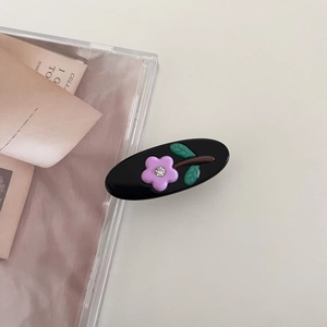 Detail of black oval hair clip featuring a purple flower and small rhinestone accent