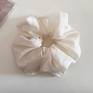Détail d'un chouchou élégant en organza crème avec un éclat doux et une texture plissée