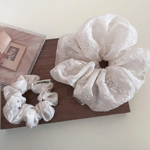 Détail macro du chouchou en organza beige avec d'élégantes textures de fleurs brodées