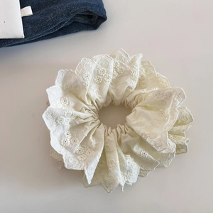 Détail d'un chouchou en dentelle double couche blanc crème avec broderie florale et bords