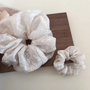 Vue détaillée des chouchous en organza beige avec broderies florales blanches sur plateau