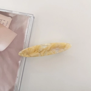 Macro detail of oval acetate hair clip in cream yellow marble finish with metal fastener