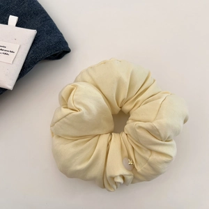 Detail of cream puff scrunchie with pink bead and golden bee charm on white surface