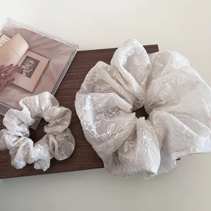 Détail de deux chouchous en organza beige avec broderies florales blanches sur plateau