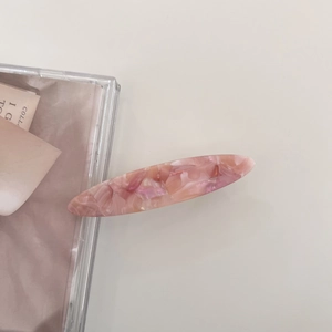 Detail of oval acetate hair clip with pink marble texture on a minimalist background