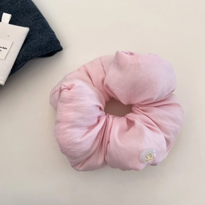 Detail of pink fabric scrunchie with white resin button and gold metal bow decoration