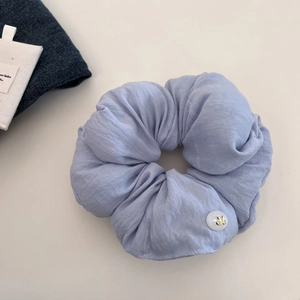 Close-up of soft light blue scrunchie with white decorative button and cotton linen texture