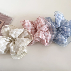 Dettaglio di tre elastici per capelli a scacchi nei colori crema, rosa e azzurro