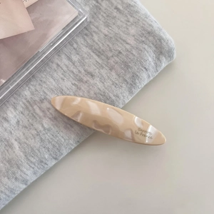 Detail view of cream marble acetate hair clip with gold Barrette la France logo lettering