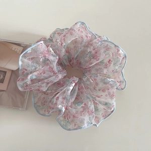Détail d'un chouchou en mousseline fleurie avec ourlet bleu et texture de tissu voile