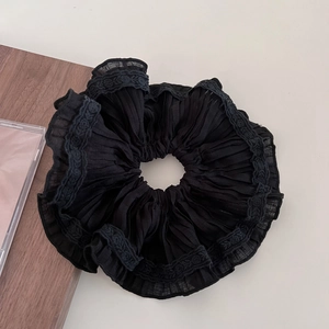 Detail shot of black pleated fabric hair tie with delicate lace edging on neutral background