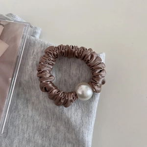 Detailed view of a champagne satin scrunchie featuring a large round white pearl accent