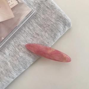 Detail view of a long oval marble pattern pink and beige acetate hair clip on soft fabric