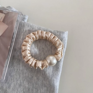 Detail of satin scrunchie with large pearl accent on grey knit fabric background