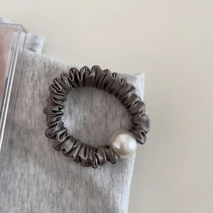 Detail of grey pleated satin hair tie with a large white pearl bead on soft fabric