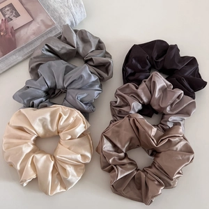 Close-up of six large satin scrunchies in neutral colors with silky glossy texture