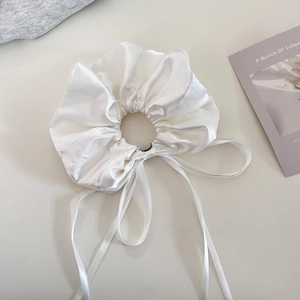 Close-up of elegant white satin scrunchie with long ribbons on a minimalist background