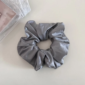 Detail view of a dark grey satin scrunchie with a soft silky glossy finish and elegant folds