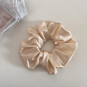 Macro detail of the champagne satin fabric hair scrunchie with a silky glossy texture