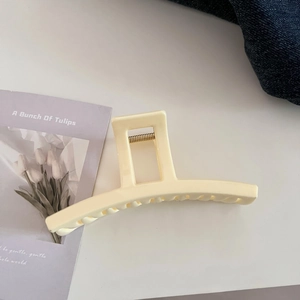 Close-up of a creamy white resin hair claw clip with golden metal spring on desk